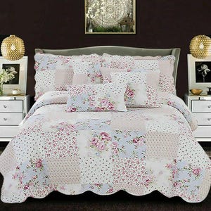 May include: A floral patchwork quilt set with a scalloped edge, featuring pink rose patterns and light blue and white polka dot designs. The set includes matching pillow shams and decorative pillows, creating a coordinated bedroom ensemble.
