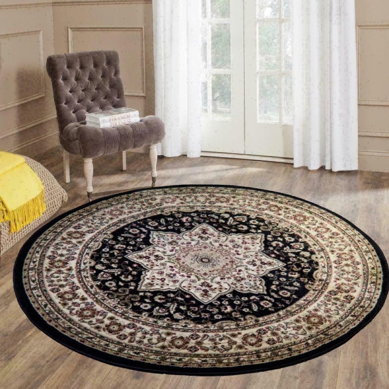 May include: A round area rug with a black border and a central medallion design. The rug features a cream-colored floral pattern on a black background, with a star-like shape in the center. The rug is placed on a hardwood floor.