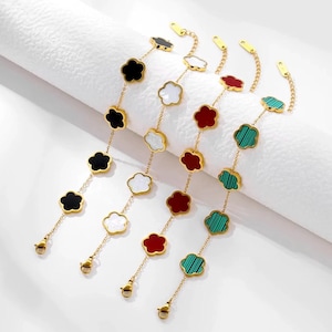 May include: Four gold bracelets featuring clover-shaped charms in black, white, red, and green. Each charm is linked by a fine gold chain. The bracelets have a lobster clasp fastening.
