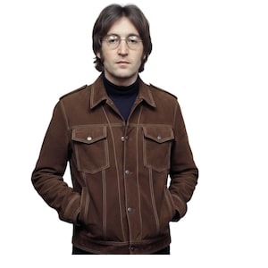 Könnte beinhalten: Braune Wildlederjacke mit weißen Nähten, zwei Brusttaschen und zwei Handtaschen. Die Jacke hat eine Knopfleiste und einen Kragen. Die Person trägt einen schwarzen Rollkragenpullover.