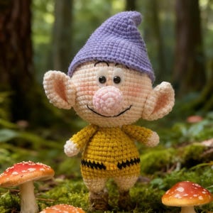 May include: A crocheted dwarf figure with a purple hat and yellow shirt stands amongst mushrooms in a forest. The dwarf has large ears, a pink nose, and a smiling expression. The scene is set on green moss. The mushrooms have red and white caps.