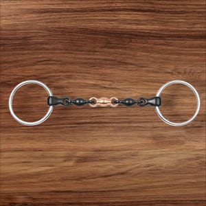 May include: A horse bit with a black and copper-colored center section and silver rings on each end. The bit is designed for use in equestrian activities. The background is a wood grain pattern.