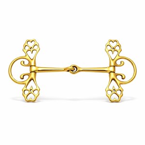Op de afbeelding: Een goudkleurige paardenbit met decoratieve hartvormige uitsparingen op de zijstukken. De bit heeft een rechte staaf in het midden en gebogen, geluste uiteinden. Het metaal heeft een gepolijst, reflecterend oppervlak en de achtergrond is wit.