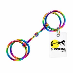 Könnte beinhalten: Ein regenbogenfarbenes Pferdgebiss mit zwei kreisförmigen Ringen und einem zentralen Verbindungsstück. Das Gebiss hat eine metallische Oberfläche und ein Etikett mit der Aufschrift "SUNSHINE BITS" und einem Logo von Pferd und Wagen.