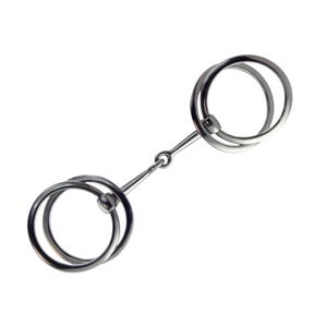 Könnte beinhalten: Ein Pferdemaulstück aus Edelstahl mit zwei großen, kreisförmigen Ringen, die durch einen Mittelsteg und einen kleinen Ring verbunden sind. Für den Reitsport.