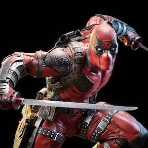 Puede incluir: Figura detallada de Deadpool en una pose dinámica, vestido con un traje rojo y negro con una máscara. La figura sostiene una katana, con detalles metálicos en los brazos y el pecho. El fondo es negro.