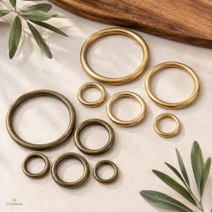Könnte beinhalten: Eine Sammlung von zehn kreisförmigen Messingringen in verschiedenen Größen mit einer glatten, polierten Metalloberfläche. Die Ringe sind verstreut angeordnet und zeigen unterschiedliche Durchmesser von klein bis groß, wobei der Text VivaBrass sichtbar ist.