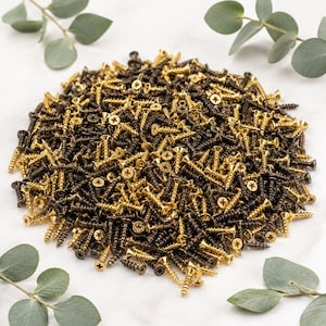May include: A large pile of small metal screws featuring a mix of shiny gold-toned and dark matte black finishes. Each screw has a threaded shank, a pointed tip, and a flat head with a cross-shaped drive recess for use with a Phillips screwdriver.