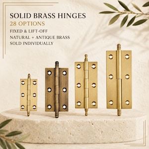 May include: Four solid brass hinges of varying sizes and finishes, including natural and antique brass. The text reads: SOLID BRASS HINGES, 28 OPTIONS, FIXED & LIFT-OFF, NATURAL + ANTIQUE BRASS, SOLD INDIVIDUALLY. Each hinge features screw holes.