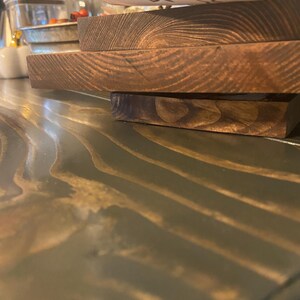 May include: A stack of three stained wooden serving boards. The boards are rectangular and have a rich, dark brown color. The wood grain is visible, adding texture. A white and gold decorated bowl is partially visible in the background.