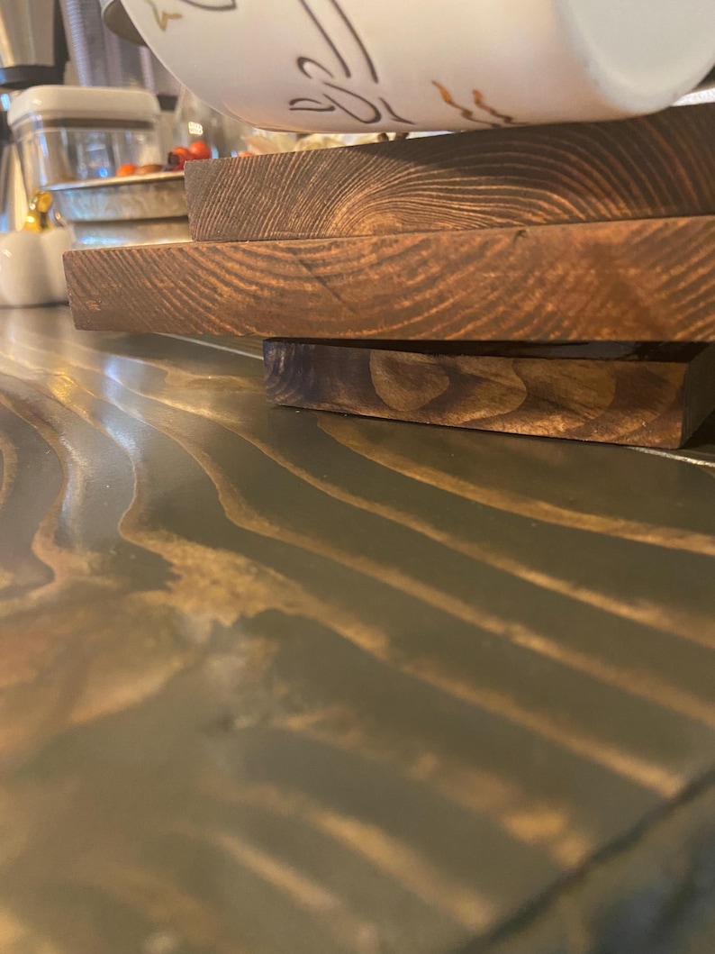 May include: A stack of three stained wooden serving boards. The boards are rectangular and have a rich, dark brown color. The wood grain is visible, adding texture. A white and gold decorated bowl is partially visible in the background.