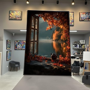 Könnte beinhalten: Großer gerahmter Leinwanddruck, der eine ruhige Herbstlandschaft zeigt. Das Kunstwerk zeigt einen Blick aus dem Fenster auf einen See, der von Bäumen mit leuchtend orangefarbenen und roten Blättern umgeben ist. Eine Teekanne steht auf einem Steinsims, mit verstreuten Blättern.