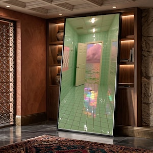 May include: A large rectangular floor mirror with a black frame displaying a surreal reflection of a mint green tiled room. The room features an open white door revealing a view of a calm ocean under a pink cloudy sky, with light reflecting on the floor.