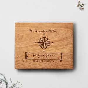 May include: A wooden plaque featuring a compass design and the phrase "There is no place like home...". The plaque includes the names "JESSICA & DAVID", the date "11.29.2025", and geographical coordinates. The design is engraved on the wood.