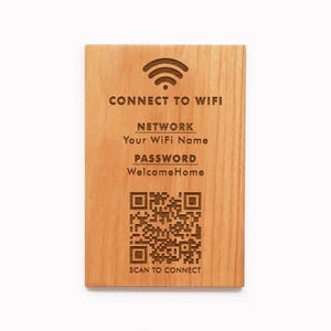Op de afbeelding: Een rechthoekig houten bord met gegraveerde tekst en een QR-code. Het bord leest "CONNECT TO WIFI", gevolgd door "NETWORK", "PASSWORD" en "SCAN TO CONNECT". Het wachtwoord is "WelcomeHome". Het bord heeft een wifi-symbool bovenaan.