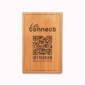 Puede incluir: Un letrero rectangular de madera con las palabras "Lets connect" y un código QR. Debajo del código QR está la palabra "INSTAGRAM" y un nombre de cuenta. El letrero es de madera marrón claro.
