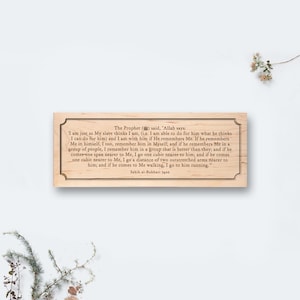 Op de afbeelding: Rechthoekige houten plaat met een decoratieve rand. De plaat bevat gegraveerde tekst uit Sahih al-Bukhari 7405, een religieuze tekst. De tekst is zwart en gecentreerd op het lichtgekleurde hout.