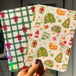 Può includere: Due cartoline rettangolari con angoli arrotondati. Una presenta un motivo a quadri verdi con piccoli fiocchi rossi. L'altra mostra un motivo festivo con maglioni verdi, alberi di Natale, candele e stivali su uno sfondo bianco.