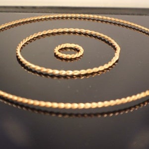 May include: Three gold-colored, twisted wire rings of different sizes. The rings are arranged in a concentric pattern, with the smallest ring in the center and the largest ring on the outside.