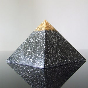 May include: A black pyramid with a gold top. The pyramid has a textured surface and is reflected in a black surface.