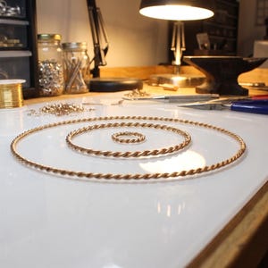 May include: Three copper-coloured, twisted wire rings of varying sizes, arranged concentrically on a white surface. A smaller ring sits in the centre. The rings are likely for jewellery making. Other jewellery-making supplies are in the background.