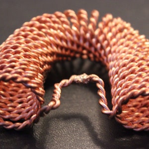 May include: A copper wire coil bracelet with a braided design. The bracelet is open and has a gap in the back.