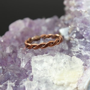 May include: A braided copper ring resting on a bed of amethyst crystals.