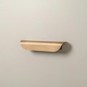 Peut inclure: Étagère incurvée en laiton, fixée au mur. La surface de l'étagère est lisse et le design est simple. Cette étagère flottante est idéale pour exposer de petits objets décoratifs. Mesure environ 30 cm de long.