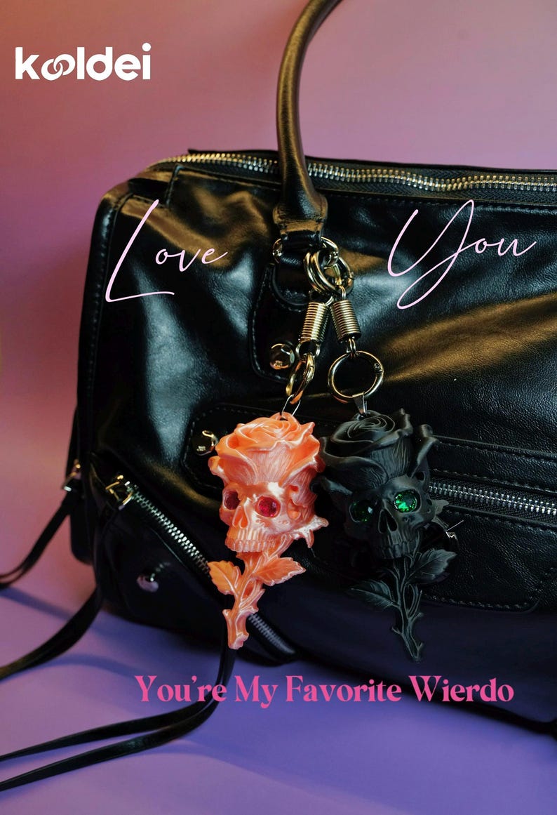 May include: Two rose skull keyrings hang from a black leather bag. One is peach with red eyes, the other is black with green eyes. The text "Love You" and "You're My Favorite Wierdo" are also visible.