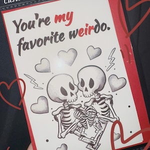 May include: Custom handwritten wish card with the text "You're my favorite weirdo." The card features a black and white illustration of two skeletons embracing, surrounded by hearts and lightning bolts, with a red border.