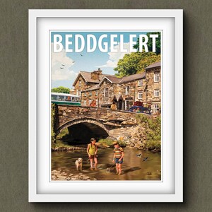 May include: Framed print of Beddgelert, a Welsh village. The image shows a stone bridge over a river, with children playing in the water. A bus and cars are on the bridge, with buildings in the background. The sky is blue.