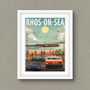 May include: A framed print of a coastal illustration, displaying the text "RHOS-ON-SEA". The artwork shows a beach scene with people, vehicles, and a boat, set against a sunny sky with clouds. The image uses a palette of blues, oranges, and greens.
