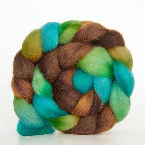 Könnte beinhalten: Nahaufnahme eines geflochtenen Strangs bunter Wollroving. Das Roving ist eine Mischung aus braunen, grünen und teal-Farben. Die Wolle ist weich und flauschig, und der Zopf ist eng gewebt. Ideal zum Spinnen oder Filzen.
