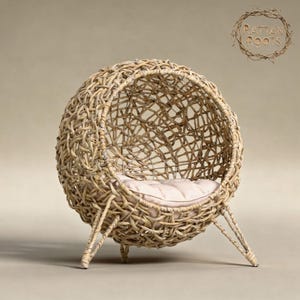 May include: A spherical pet bed made from woven rattan. The bed is a light beige colour and has a soft, light pink cushion inside. It is supported by three angled legs. The text "Rattan Roots" is in a circular design in the upper right corner.