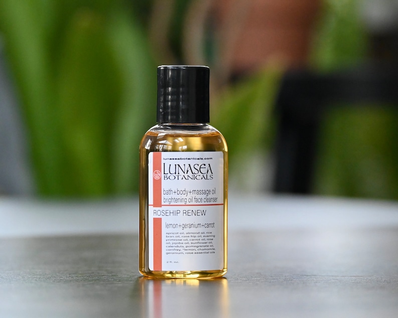 May include: A small amber glass bottle with a black cap and a white label. The label reads "LUNASEA BOTANICALS bath+body+massage oil brightening oil face cleanser ROSEHIP RENEW lemon+geranium+carrot"