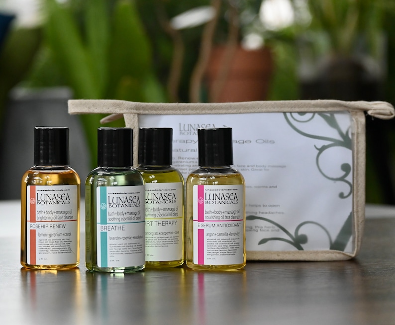 May include: Four small glass bottles with black caps and labels containing bath and body massage oils. The bottles are arranged in a row on a wooden surface. The labels feature the brand name "LUNASEA BOTANICALS" and the names of the oils: "ROSEHIP RENEW", "BREATHE", "SPORT THERAPY", and "E SERUM ANTIOXIDANT". The bottles are in a small, beige canvas bag with a zipper.