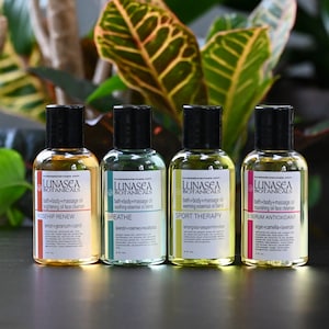 May include: Four amber glass bottles with black lids and white labels. The labels have the text "LUNASEA BOTANICALS" and list different bath and body oil blends: "ROSEHIP RENEW", "BREATHE", "SPORT THERAPY", and "ESERUM ANTIOXIDANT".