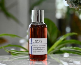 May include: A brown glass bottle with a silver lid and a white label that reads "LUNASEA BOTANICALS LAVENDER CEDARWOOD grounding body cleanser with olive leaf and white tea lavender+cedarwood+jasmine".