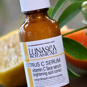 K&ouml;nnte beinhalten: Eine Glasflasche mit LunaSea Botanicals Citrus C Serum, einem Vitamin-C-Gesichtsserum zur Aufhellung und Korrektur von Pigmentflecken. Das Etikett hat einen wei&szlig;en Hintergrund mit schwarzem Text und ein kleines Logo mit einem Kreis und einem Blatt darin. Die Flasche steht auf einem Tisch mit einer Zitrone und einer Orange im Hintergrund.