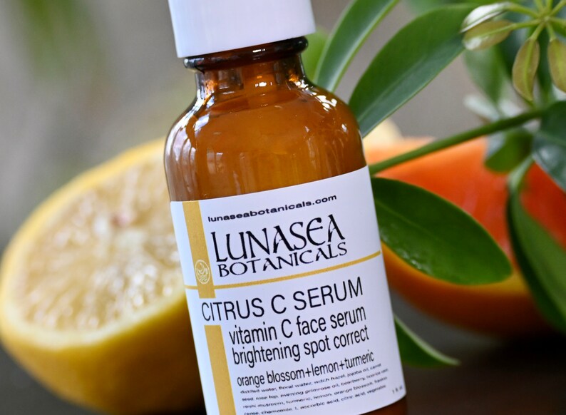 K&ouml;nnte beinhalten: Eine Glasflasche mit LunaSea Botanicals Citrus C Serum, einem Vitamin-C-Gesichtsserum zur Aufhellung und Korrektur von Pigmentflecken. Das Etikett hat einen wei&szlig;en Hintergrund mit schwarzem Text und ein kleines Logo mit einem Kreis und einem Blatt darin. Die Flasche steht auf einem Tisch mit einer Zitrone und einer Orange im Hintergrund.