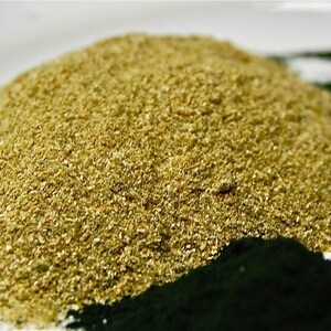 May include: A close-up of a pile of light green powder, possibly a supplement or food ingredient. The powder is in a bowl and there is a dark green powder in the background.