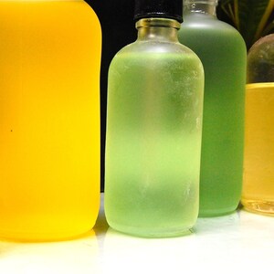 May include: Four glass bottles with different colored liquids. The bottles are clear and have a variety of shapes. The liquids are green, yellow, and a light amber color.