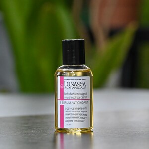 May include: A small, clear glass bottle with a black cap, containing a yellow liquid. The bottle is labeled "LUNASEA BOTANICALS" and "E SERUM ANTIOXIDANT argan+camellia+lavender".