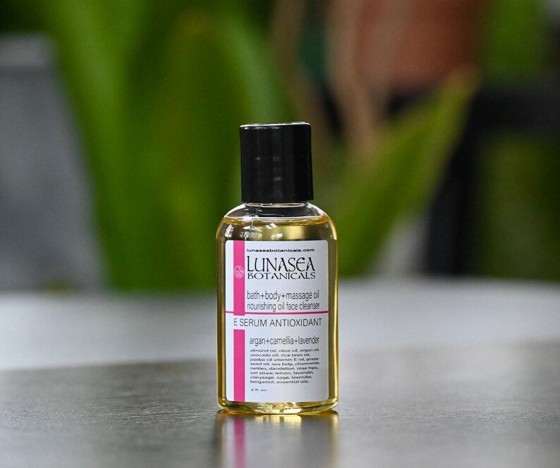 May include: A small, clear glass bottle with a black cap, containing a yellow liquid. The bottle is labeled "LUNASEA BOTANICALS" and "E SERUM ANTIOXIDANT argan+camellia+lavender".