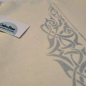 Könnte beinhalten: Nahaufnahme eines cremefarbenen Stoffes mit einem hellblauen keltischen Knotenmuster, das in der Ecke aufgedruckt ist. Ein kleines Etikett mit dem Text "ColorBoo" befindet sich in der oberen linken Ecke. Der Stoff hat ein strukturiertes Aussehen.