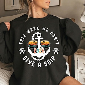 May include: Black sweatshirt with a white anchor design, sunglasses, and the text "THIS WEEK WE DON'T GIVE A SHIP 2026". The sunglasses feature a sunset scene with palm trees and a cruise ship. The design includes nautical elements.