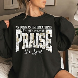 May include: Black sweatshirt with the text "AS LONG AS I'M BREATHING I've got a reason to PRAISE the Lord" in white and gold lettering. The sweatshirt has long sleeves and a crew neck.