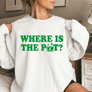 以下が含まれることがあります： 緑色の「WHERE IS THE POT?」の文字と、クローバーの付いた金のポットが描かれた白いスウェットシャツ。聖パトリックの日のために最適な、カジュアルなトップスです。