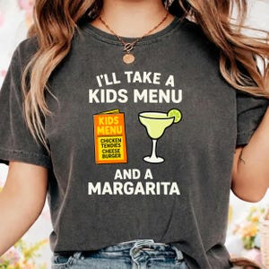 Puede incluir: Camiseta gris oscuro con el texto "I'll Take a Kids Menu and a Margarita". El diseño incluye una imagen de dibujos animados de un menú infantil y una copa de margarita con una rodaja de lima. El menú enumera tenders de pollo, queso y una hamburguesa.