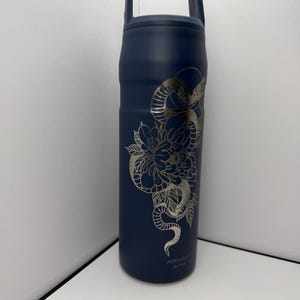 May include: Navy blue insulated water bottle with a silver floral and snake design. The bottle has a handle and a screw-on lid. The design wraps around the bottle, featuring a detailed flower and snake illustration.
